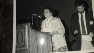 Joan Iversen at podium, Mark Delligatti to the right